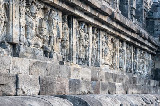 Ancient stone carvings on a temple wall, depicting standing and seated human figures. photo