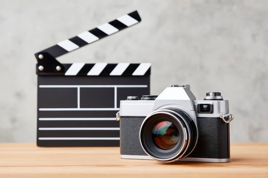Vintage camera positioned on wooden table beside a classic film clapperboard, showcasing the essence of photography and filmmaking in a creative workspace environment photo