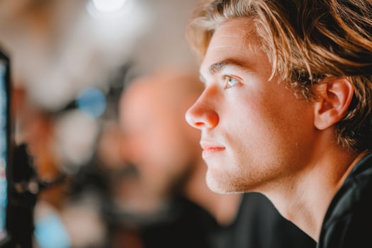 Young man with light brown hair is focused on a computer screen in a modern workspace, showcasing concentration and engagement in a creative environment photo