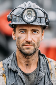 Male miner with blue eyes, wearing a hard hat and work clothes, stands confidently in a mining environment, showcasing dedication and resilience in the mining industry photo