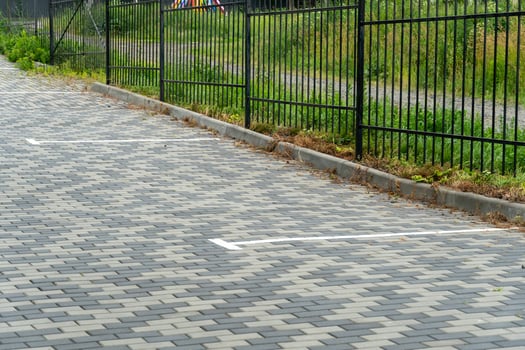A neatly paved parking area features clearly marked spaces, bordered by a black metal fence and green grass. The setting appears tranquil and well-maintained photo
