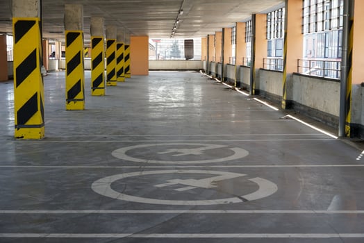A spacious parking garage features clear directional markings with yellow stripes. Natural light filters in through large windows, creating a bright atmosphere photo