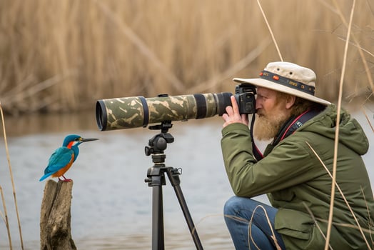 A man with a camera and a bird on a tripod photo