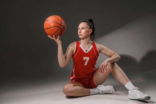 Confident Female Basketball Player Sitting with Ball in Red Uniform after Training on Court photo