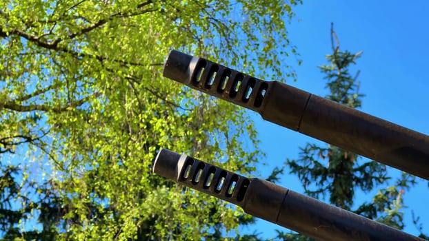 A detailed view showcasing various firearm muzzles beautifully juxtaposed against lively greenery and a clear blue sky photo
