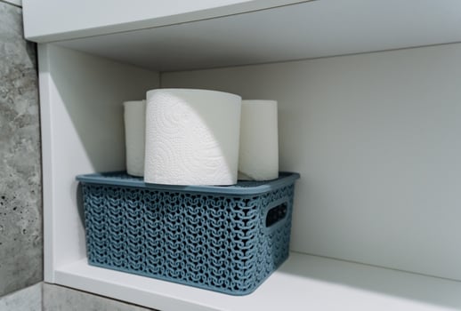 Atop a shelf, there is a blue basket containing a total of three rolls of toilet paper, highlighting a practical and organized way to store household supplies neatly and efficiently photo