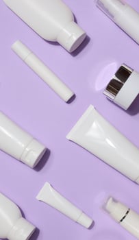 Variety of white plastic tubes and bottles with cosmetics arranged randomly on a lavender background. Top view photo