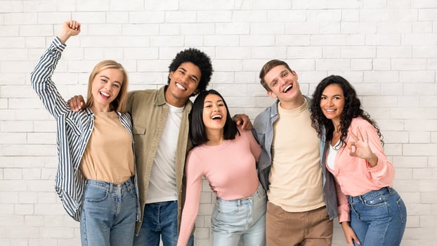Have fun with friends and get education in college or university. Happy young multiethnic people team in casual hugging and looking at camera, on white brick wall background, studio shot photo