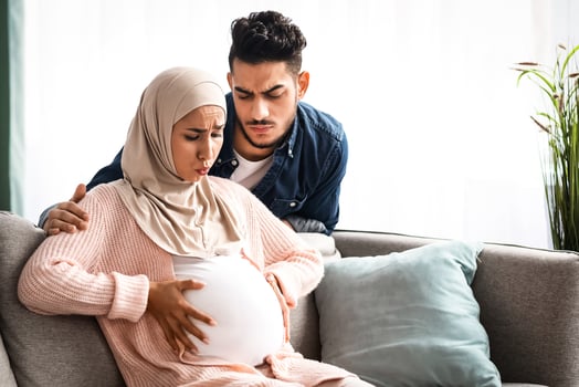 Prenatal Contractions. Caring arab husband comforting his pregnant muslim wife that suffering from abdominal pain at home, young woman having cramps, getting ready for delivery, copy space photo