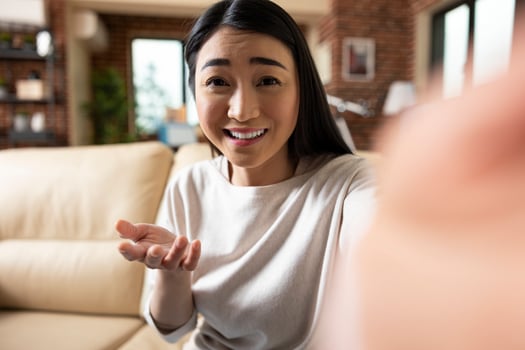 Female entrepreneur smiling and engaging during livestream at home, gestures to camera, sharing business ideas. Businesswoman connecting with followers through friendly, joyful online content. photo