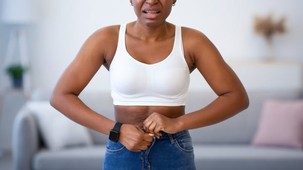 Frustrated Black Woman Buttoning Small Jeans After Weight Gain Standing At Home, Looking At Camera. Slimming Issue, Visceral Fat And Cellulitis, Weight-Loss Problem Concept photo