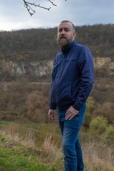 Man stands on a hillside overlooking a scenic valley during a cloudy day in nature photo