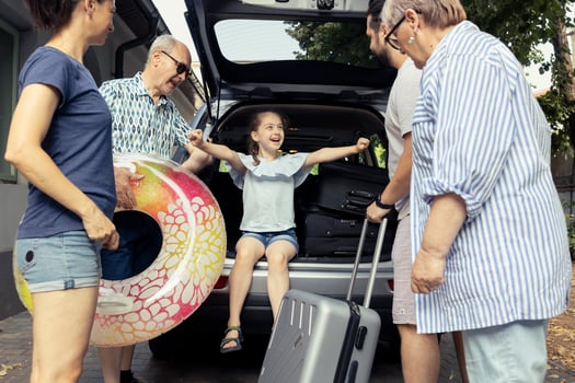 Excited little child smiles as the parents and grandparents pack the car for a road trip. Big relaxed family boding during a summertime fun holiday, the joy of travelling together. photo