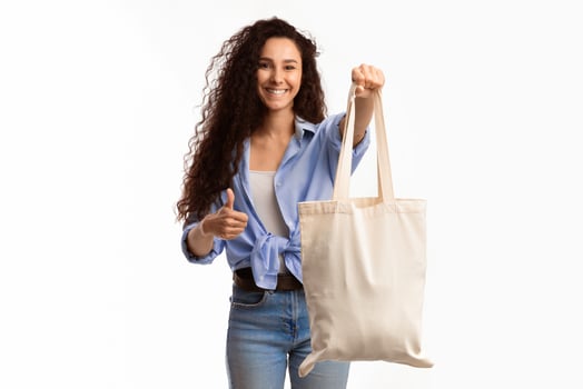 Cheerful Millennial Lady Showing White Cotton Shopper Bag Gesturing Thumbs Up In Approval Standing Over White Studio Background. Lady With Textile Handbag Approving Eco-Friendly Lifestyle With Like photo
