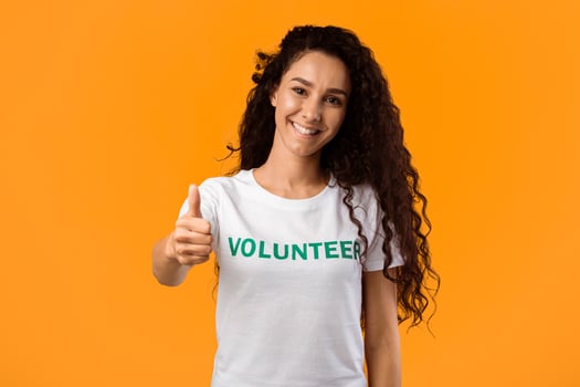Volunteer Woman Showing Like Gesturing Thumbs Up Standing On Yellow Studio Background, Smiling To Camera. I Approve Charity Work And Volunteering Concept photo