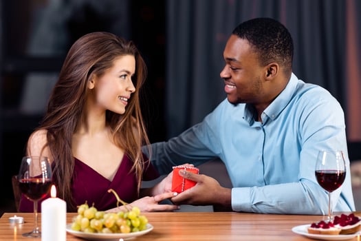 Romantic Date. Loving Black Man Giving Gift Box To His White Girlfriend, Greeting Her With Anniversary Or International Women's Day, Affectionate Multiracial Couple Having Dinner In Restaurant photo