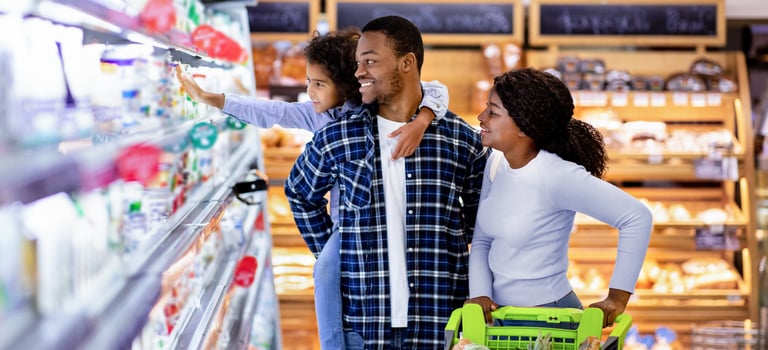 Portrait of happy black family with trolley shopping together at grocery store. Millennial African American parents with lovely daughter picking food, choosing milk products at big mall photo