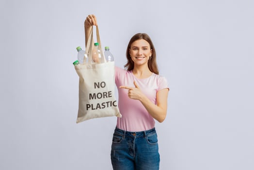 Eco Tote Bag With No More Plastic Incription In Hands Of Young Smiling Woman. Positive Millennial Volunteer Lady Enjoying Garbage Sorting And Recycling, Standing On Light Studio Background, Free Space photo