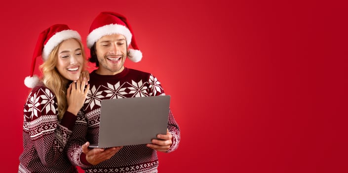 Lovely lady and her boyfriend in winter outfits shopping for Christmas gifts online on laptop, red background photo
