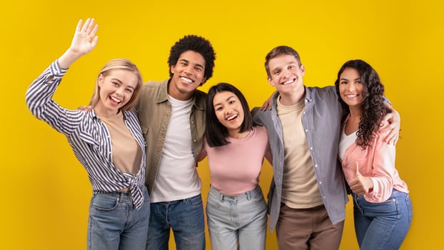 Education at university or college abroad. Cheerful young multiracial international students have fun, laughing, hugging and waving to camera isolated on orange background, copy space, studio shot photo