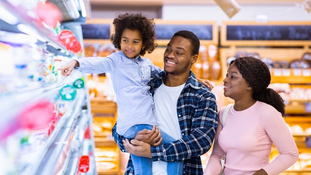 Happy black parents and their pretty daughter with shopping cart having fun buying groceries at hypermarket. African American family purchasing dairy products at modern mall photo