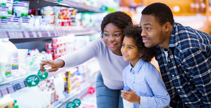 Happy African American family buying milk products at modern supermarket, empty space. Millennial black parents and their daughter purchasing groceries at mall, choosing fresh food photo