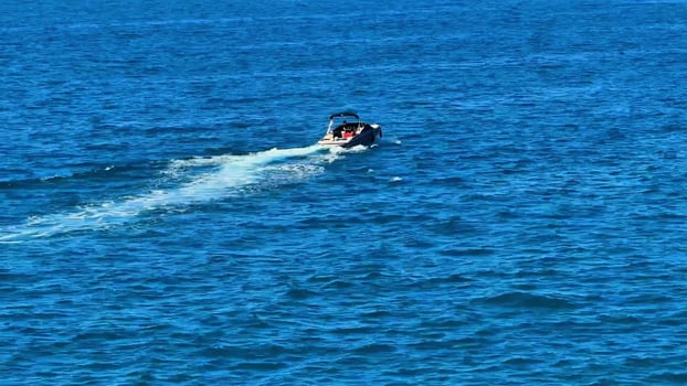 A sleek motorboat effortlessly glides gracefully across the shimmering blue water, leaving behind a gentle wake photo