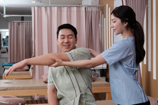 Asian middle-aged male patient is arms stretching, treated health recovery for shoulder muscle pain relief by a physical therapist doctor, passive medical therapy at massaging wellness spa clinic. photo