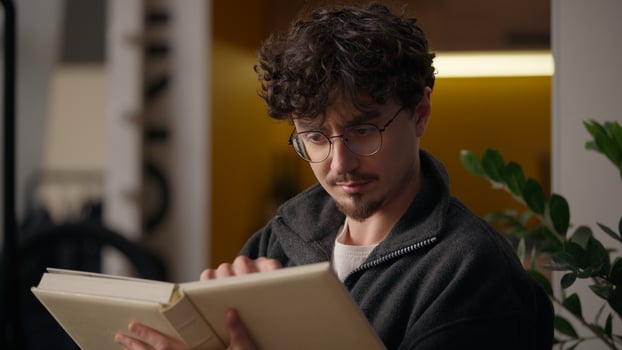 Focused Hispanic guy reader bookworm reading book literature at home man hobby leisure male relaxing learner study enjoying read fiction looking notebook page paper learning information text education photo