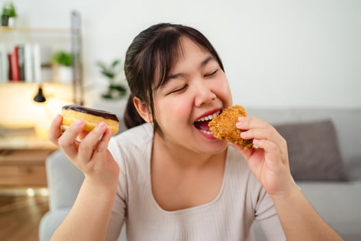 Asian woman happily eating fried chicken and donuts, unhealthy food, junk food, weight gain photo