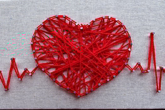 Red heart and heartbeat lines string art made with tangled red yarn on metal nails at canvas texture photo