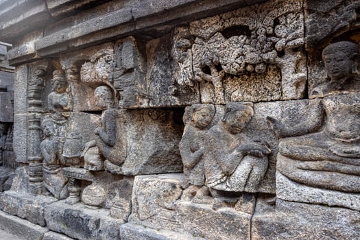 Ancient stone relief showing people, trees, and intricate carvings on a temple wall. photo
