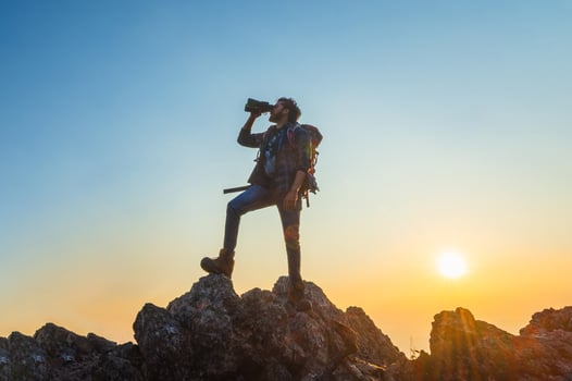 man is standing on a mountain top, looking through a camera lens photo