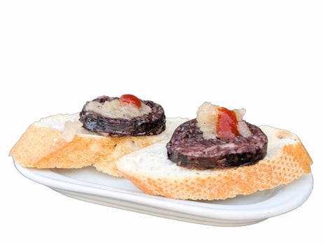 Savory blood sausage topped with onion and sauce on crusty bread served on a white plate photo