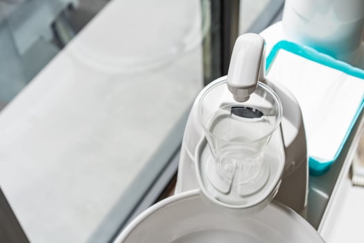 A plastic glass on a cup holder of the modern ceramic mouth cleaning sink in the dentist office near a window,a photo