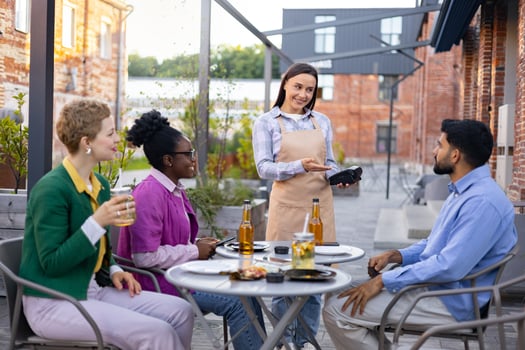 A female waiter presents a portable terminal to a customer, ready to process a payment at an outdoor cafe. photo
