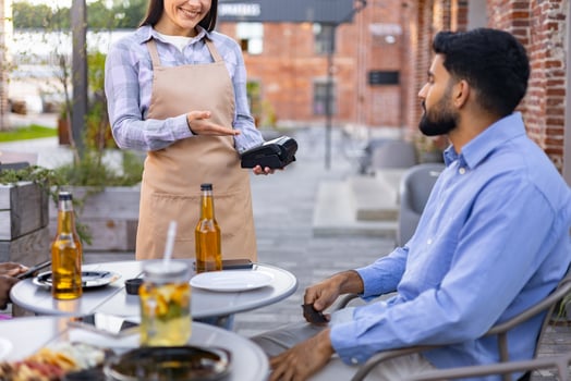 A female waiter offers a payment terminal to a customer at an outdoor restaurant table. photo