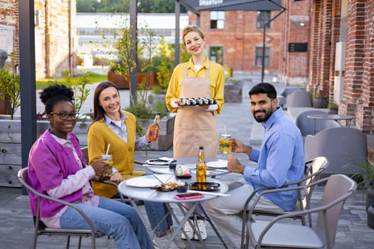 Diverse group of friends enjoying sushi and drinks at an outdoor restaurant, served by a friendly waitress. photo