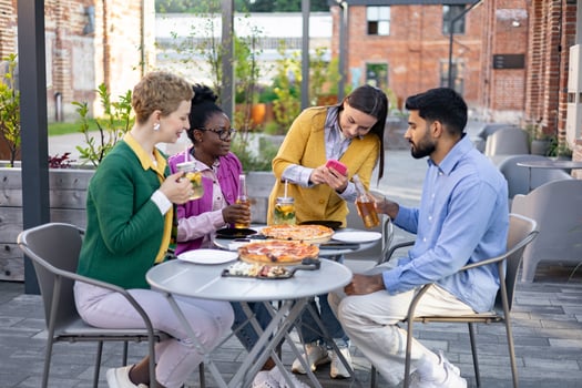 A diverse group of friends enjoys pizza and drinks while taking a picture on a sunny day at an outdoor restaurant. photo