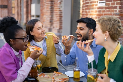 A diverse group of friends happily eating pizza together outdoors, enjoying a meal and each other's company. photo