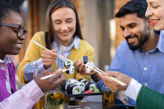 A diverse group of friends enjoys sushi at an outdoor restaurant, using chopsticks and smiling. photo