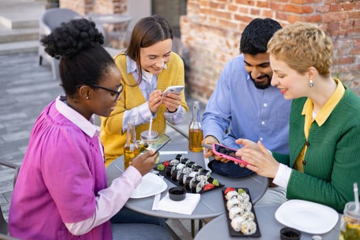 A diverse group of friends enjoy sushi and drinks while using their smartphones at an outdoor cafe. photo
