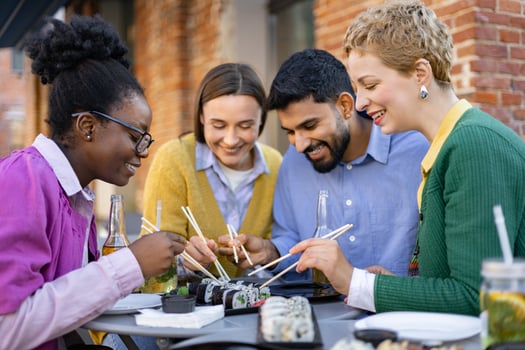 Diverse group of friends enjoying sushi together at an outdoor restaurant, sharing food and laughter. photo