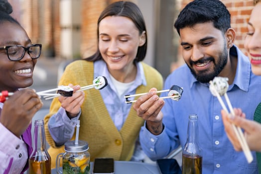 A diverse group of friends are enjoying sushi together outdoors, smiling and laughing while eating. photo