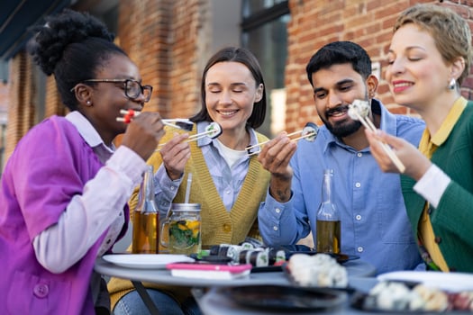 Diverse group of friends enjoying sushi and drinks outdoors, creating a relaxed and joyful dining experience. photo