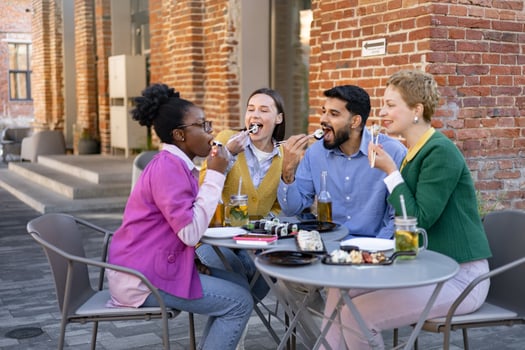 Group of diverse friends enjoying sushi and drinks outdoors at a restaurant, laughing and having a great time. photo