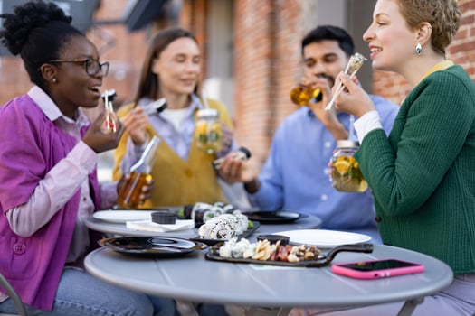 A diverse group enjoys sushi and drinks at an outdoor table, laughing and engaging in conversation. photo