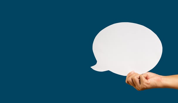 Hand holding a blank white speech bubble while standing against a blue background. photo