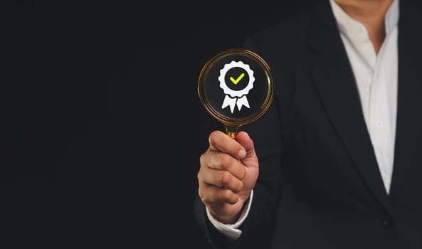 Businessman holding a magnifying glass with the best quality symbol assurance icon while standing against a black background photo