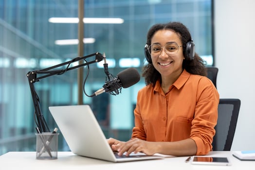 An African American woman smiles while working on a podcast with a microphone and laptop at a modern office. photo